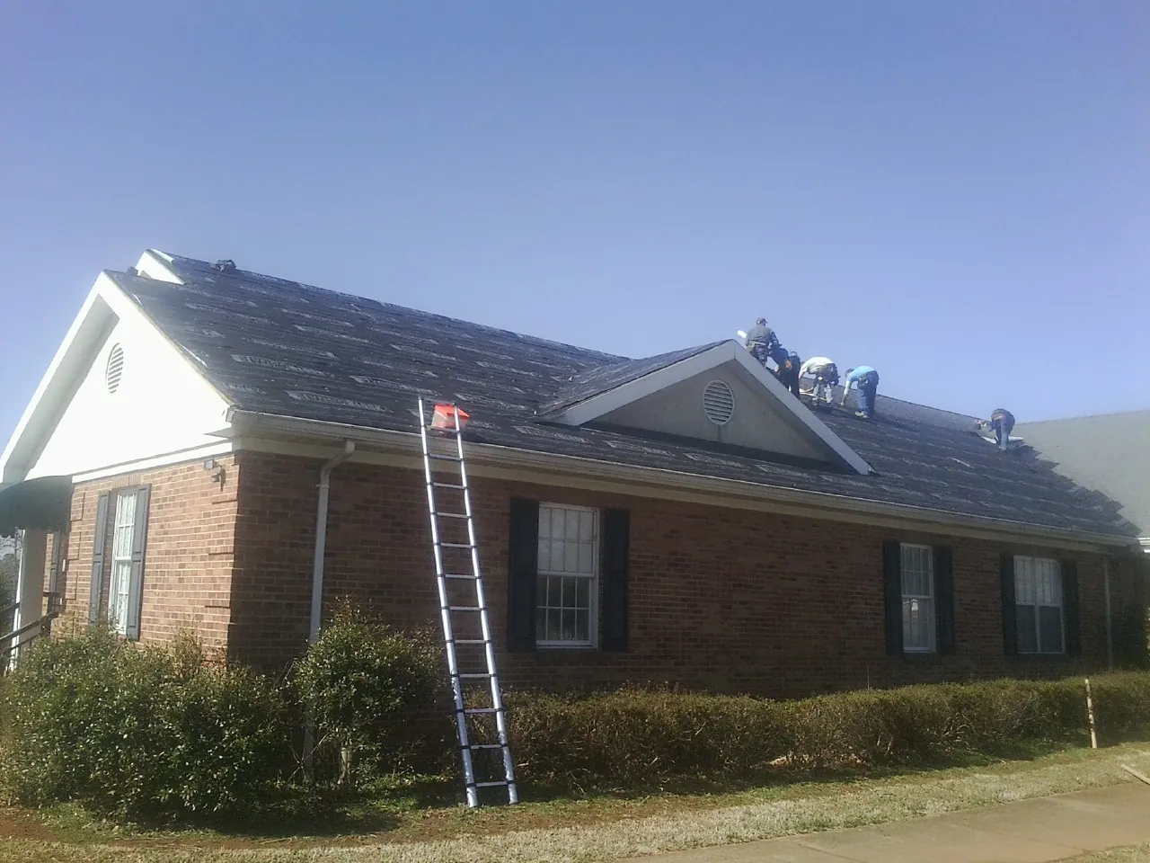 Crew tearing shingles off a brick ranch roof with a ladder set — Emergency Roof Repair work by our crew in San Marino