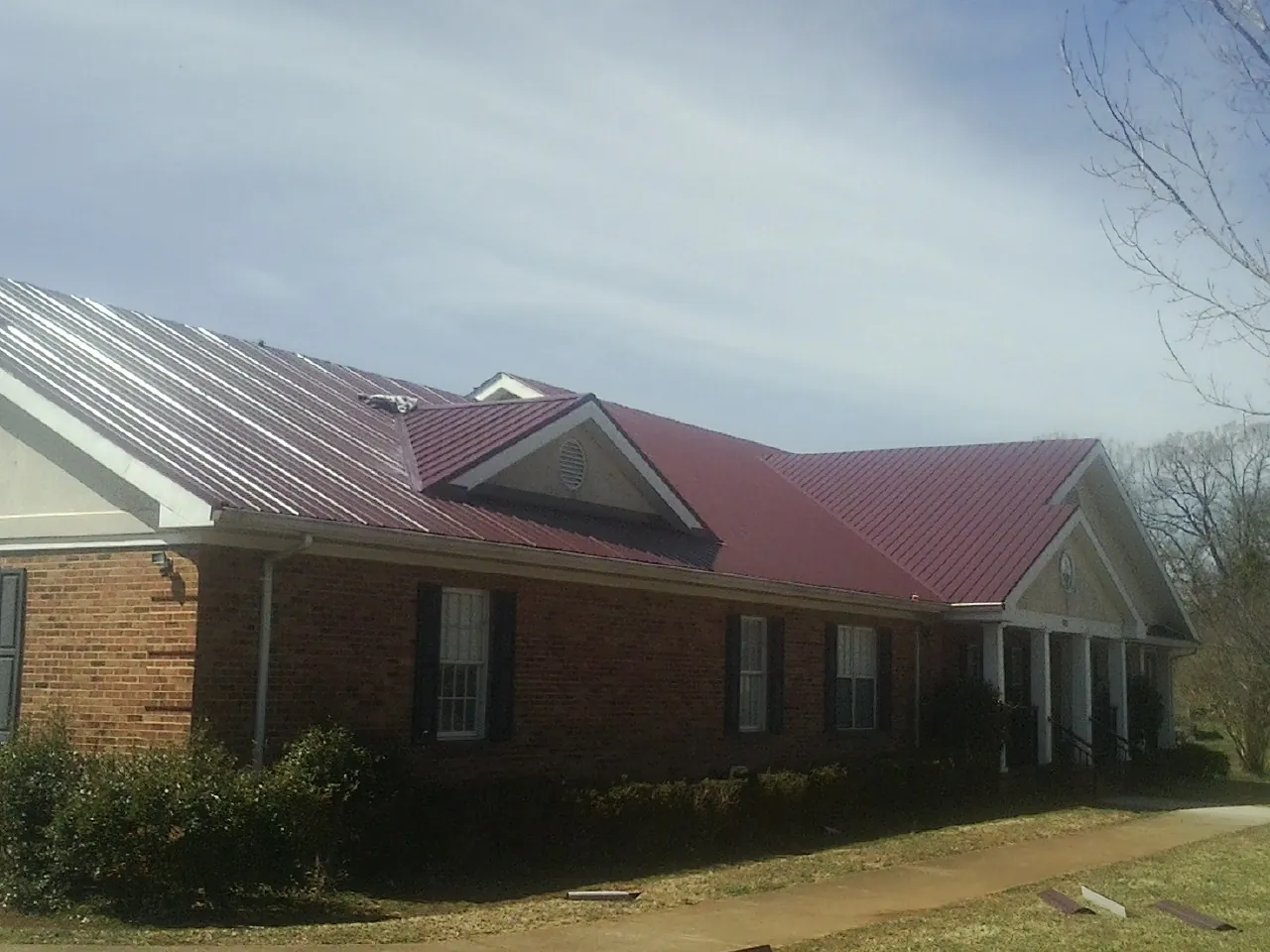 Red metal roof with gabled entries on a long brick building, from a Hail Damage Roof Repair job in San Marino