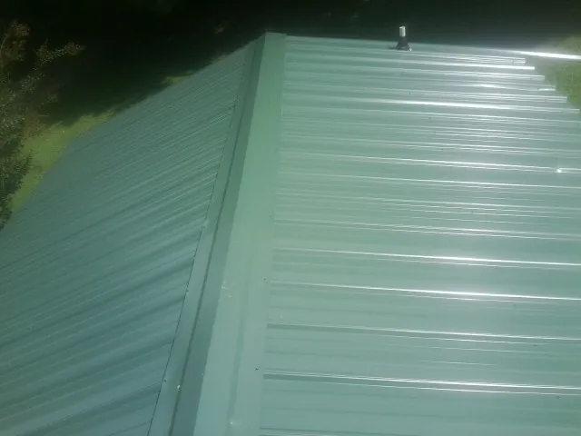 New green metal panels meeting at the ridge of a roof — Flat Roof Repair work by our crew in San Marino
