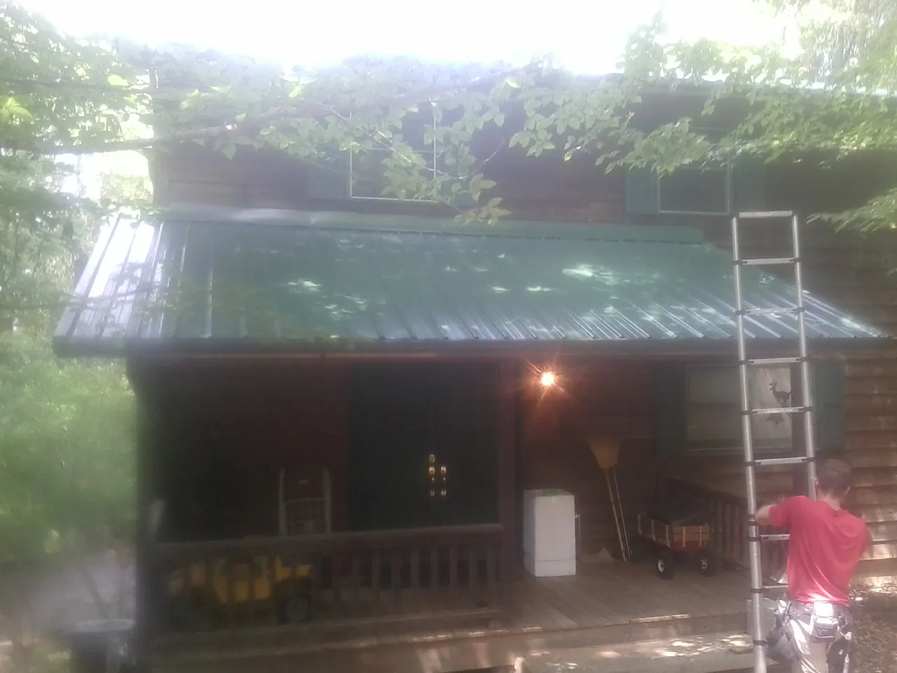 Worker on a ladder at the green porch roof of a wooded cabin in San Marino