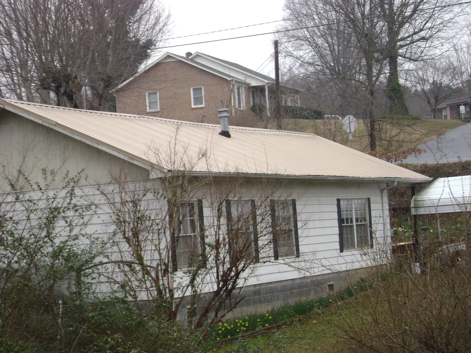 Tan metal roof on a white sided house set into a hillside — Commercial Roofing by Roofing Brothers in San Marino